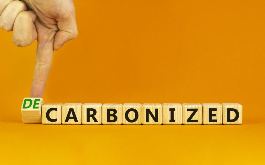 Carbonized or decarbonized symbol. Businessman turns a wooden cube and changes words 'carbonized' to 'decarbonized'. Orange background, copy space. Business, Carbonized or decarbonized concept.