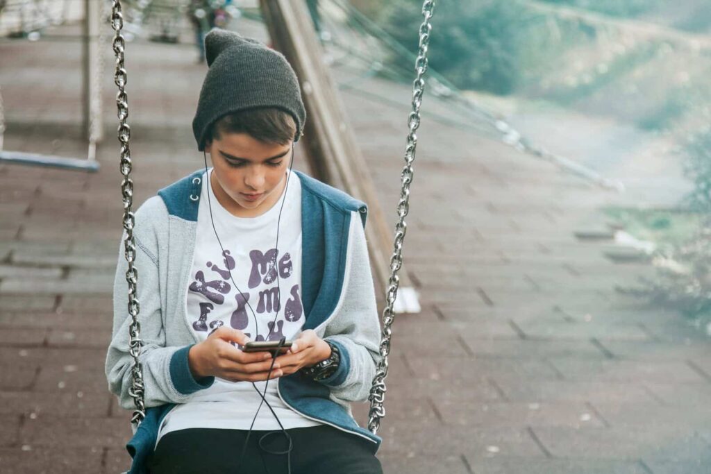 child with mobile phone on swing on city street